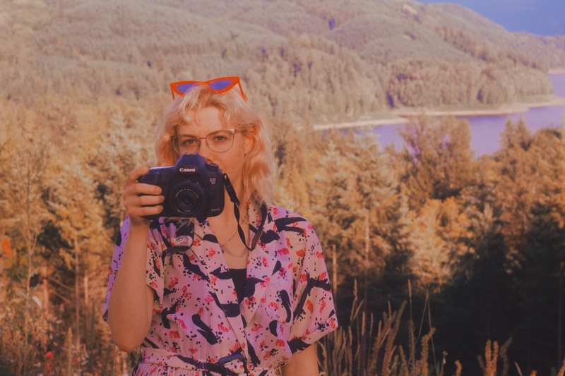 Hayley holding her camera in front of a scenic view of the Pacific Northwest forest and water